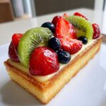 Close-up of a rectangular slice of Fresh Fruit Tart with Vanilla Pastry Cream, topped with glazed strawberries, kiwi, and blueberries.