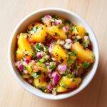 Overhead close-up of a white bowl filled with vibrant Fresh Peach Salsa for Chips or Grilling, featuring diced peaches and red onion.