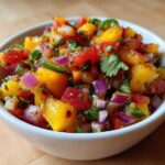 Close-up of vibrant Fresh Peach Salsa featuring diced peaches, red onion, and cilantro in a white bowl.