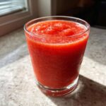 Close-up of a bright red, icy Frozen Strawberry Daiquiri Recipe served in a clear glass on a countertop.