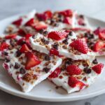 Close-up of broken pieces of Frozen Yogurt Bark topped with fresh strawberries, chocolate chips, and granola.