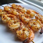 Close-up of perfectly cooked Garlic Butter Grilled Shrimp Skewers seasoned with herbs and spices, resting on a white plate.