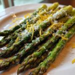 Close-up of perfectly Grilled Asparagus Spears with Parmesan and Lemon zest on a white plate.