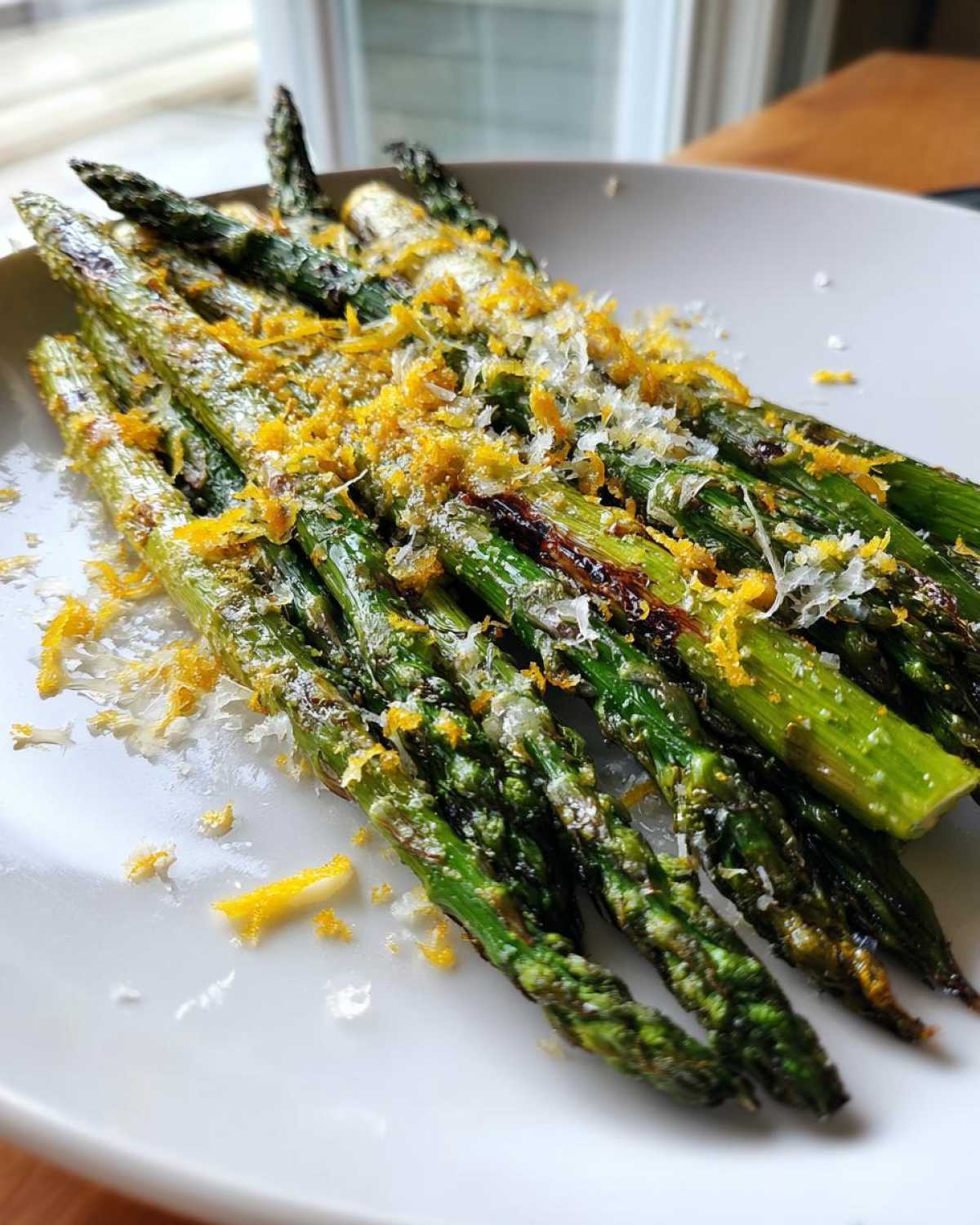 Close-up of perfectly cooked Grilled Asparagus Spears with Parmesan and Lemon zest on a white plate.