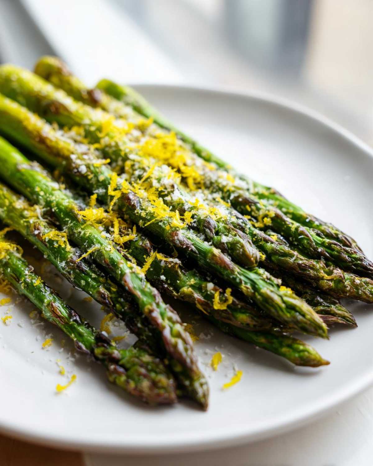 Close-up of perfectly grilled asparagus spears topped with grated Parmesan and bright yellow lemon zest.