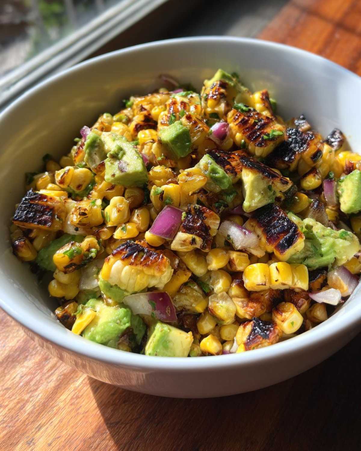 Close-up of vibrant Grilled Corn and Avocado Salsa featuring charred corn kernels, diced avocado, and red onion in a white bowl.