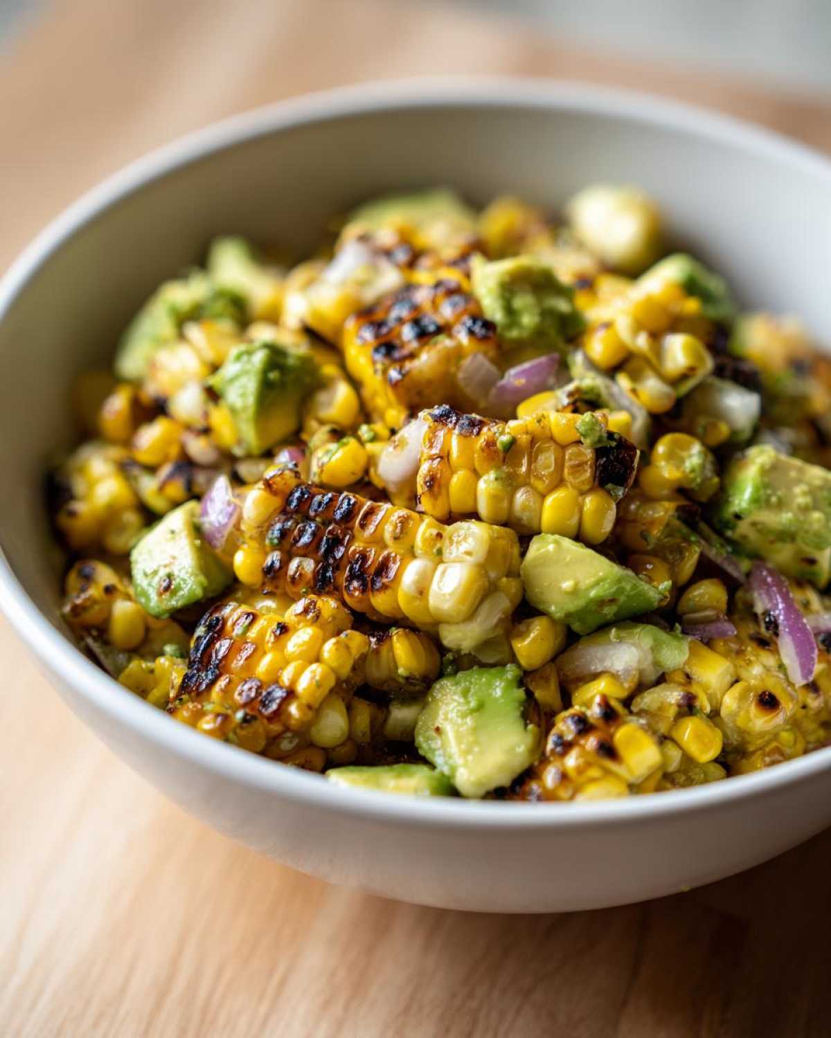 Close-up of Grilled Corn and Avocado Salsa featuring charred corn kernels, diced avocado, and red onion in a white bowl.