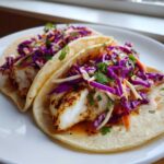 Two delicious Grilled Fish Tacos with chipotle slaw piled high with purple cabbage and cilantro.