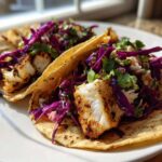 Two Grilled Fish Tacos topped with flaky white fish and bright purple chipotle slaw.