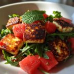 Close-up of Grilled Halloumi Salad featuring seared halloumi cheese, bright red watermelon chunks, and fresh mint on a bed of arugula.