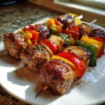 Close-up of two Grilled Italian Sausage and Bell Pepper Skewers on a white plate, showing charred sausage balls and colorful peppers.