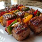 Close-up of perfectly charred Grilled Italian Sausage and Bell Pepper Skewers resting on a white plate.