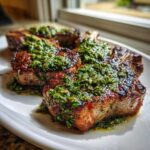 Close-up of perfectly seared Grilled Lamb Chops with Mint Chimichurri spooned generously over the top.