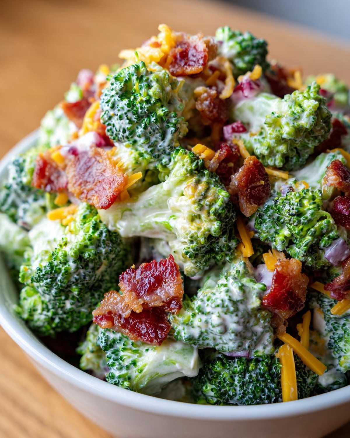 Close-up of a bowl filled with Hearty Broccoli Salad with Bacon and Cheddar Cheese, coated in creamy dressing.