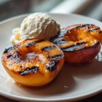 Two halves of Honey Grilled Peaches topped with a scoop of vanilla ice cream on a white plate.