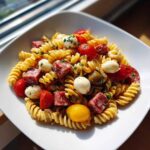 A close-up of Italian Antipasto Pasta Salad featuring rotini pasta, cubed salami, mozzarella balls, and cherry tomatoes.