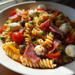 Close-up of Italian Antipasto Pasta Salad featuring rotini pasta, salami slices, mozzarella balls, and cherry tomatoes.