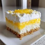 A perfect square slice of Layered Lemon Lush Dessert featuring a graham cracker crust, creamy white layer, bright lemon curd, and whipped topping.