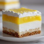 Close-up of a perfect square slice of Layered Lemon Lush Dessert showing graham cracker crust, white cream layer, and bright lemon topping.