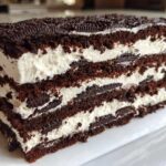 Close-up of a thick slice of Layered Oreo Icebox Cake showing alternating dark chocolate cake and white cream layers.