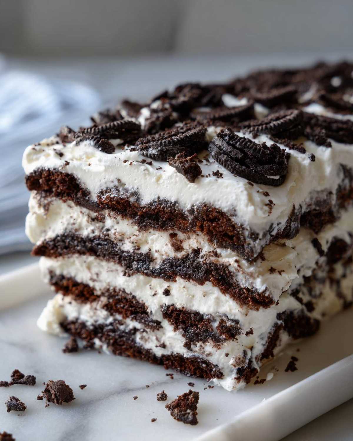 A rich, multi-layered slice of Layered Oreo Icebox Cake showing alternating dark cookie layers and white cream filling.
