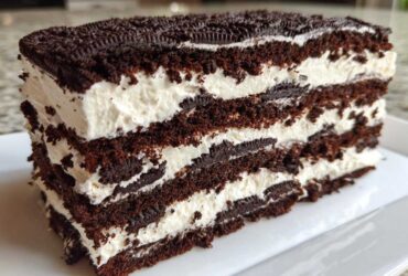 Close-up of a thick slice of Layered Oreo Icebox Cake showing alternating dark chocolate cake and white cream layers.