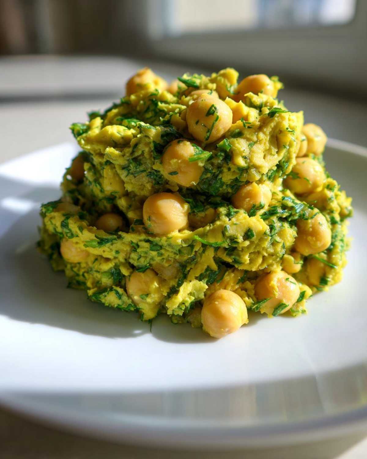 A mound of bright yellow Lemony Chickpea Salad with Herbs, studded with whole chickpeas, served on a white plate.