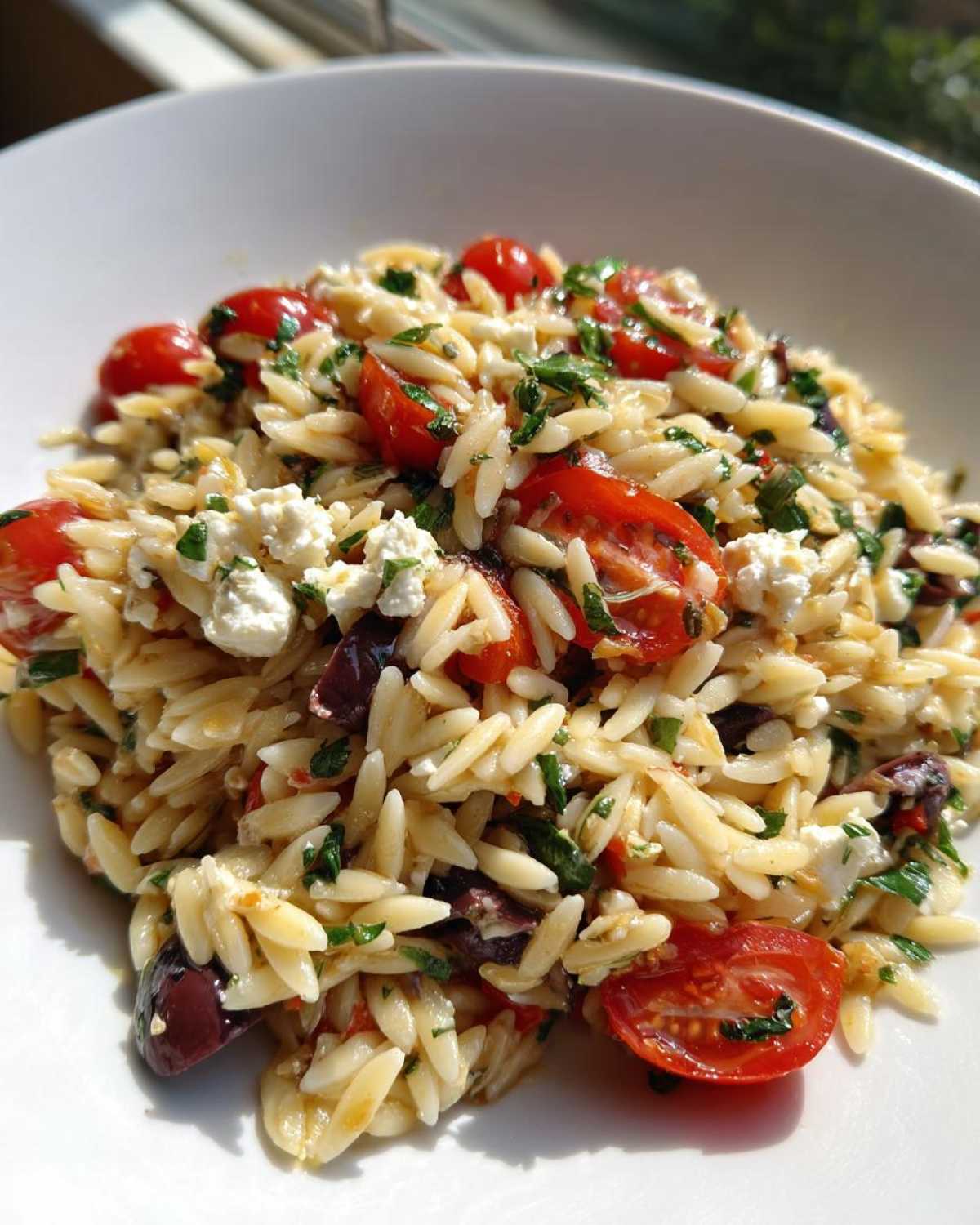 A close-up of a bright Mediterranean Orzo Salad featuring orzo pasta, halved cherry tomatoes, feta cheese, and olives.