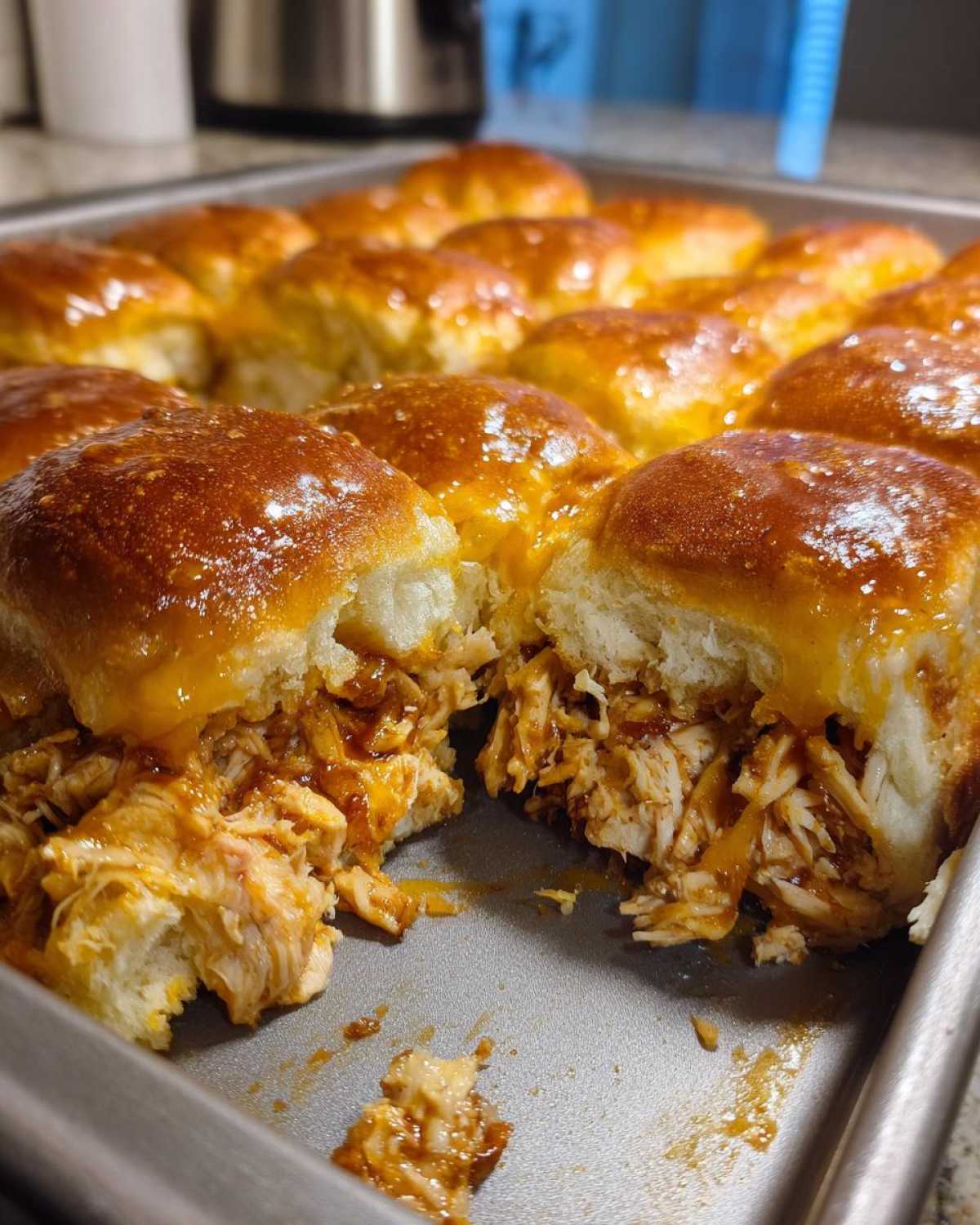 A close-up view of freshly baked Mini BBQ Chicken Sliders, showing shredded chicken filling and shiny, glazed tops.