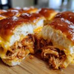 A close-up view of a batch of cheesy Mini BBQ Chicken Sliders, showing pulled chicken filling and glossy tops.