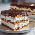 Close-up of a layered slice of No-Bake Chocolate Eclair Cake Dessert with graham crackers, white cream, and chocolate topping.