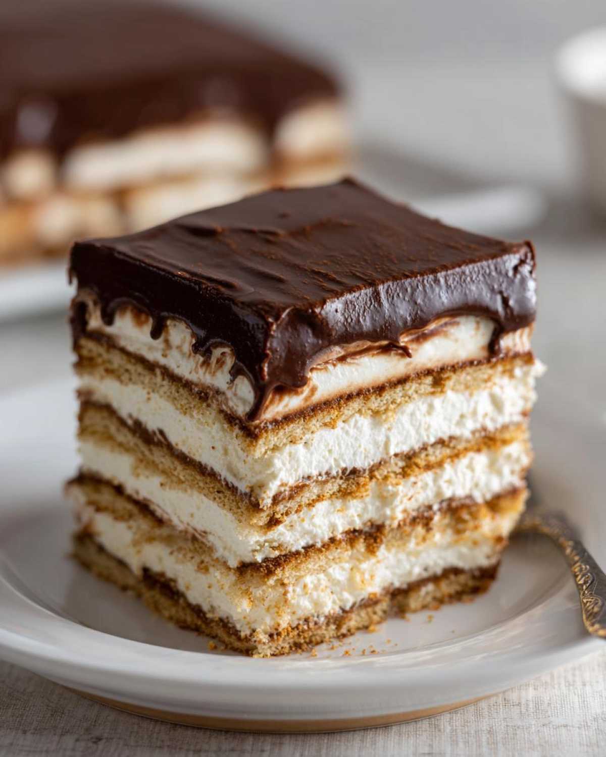 A perfect square slice of No-Bake Chocolate Eclair Cake Dessert showing multiple layers of cream and graham crackers topped with chocolate ganache.