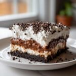 A square slice of No-Bake Chocolate Lasagna Dessert showing four distinct layers topped with whipped cream and mini chocolate chips.