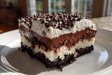 A decadent slice of No-Bake Chocolate Lasagna Dessert showing four distinct layers topped with whipped cream and mini chocolate chips.