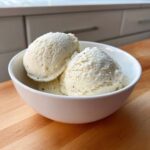 Three scoops of creamy No-Churn Vanilla Bean Ice Cream speckled with black vanilla seeds in a white bowl.