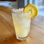 A tall glass filled with ice and Old-Fashioned Homemade Lemonade, garnished with a fresh lemon slice.