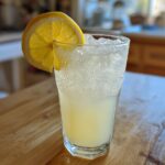 A tall glass filled with ice and sparkling Old-Fashioned Homemade Lemonade Recipe, garnished with a fresh lemon slice.