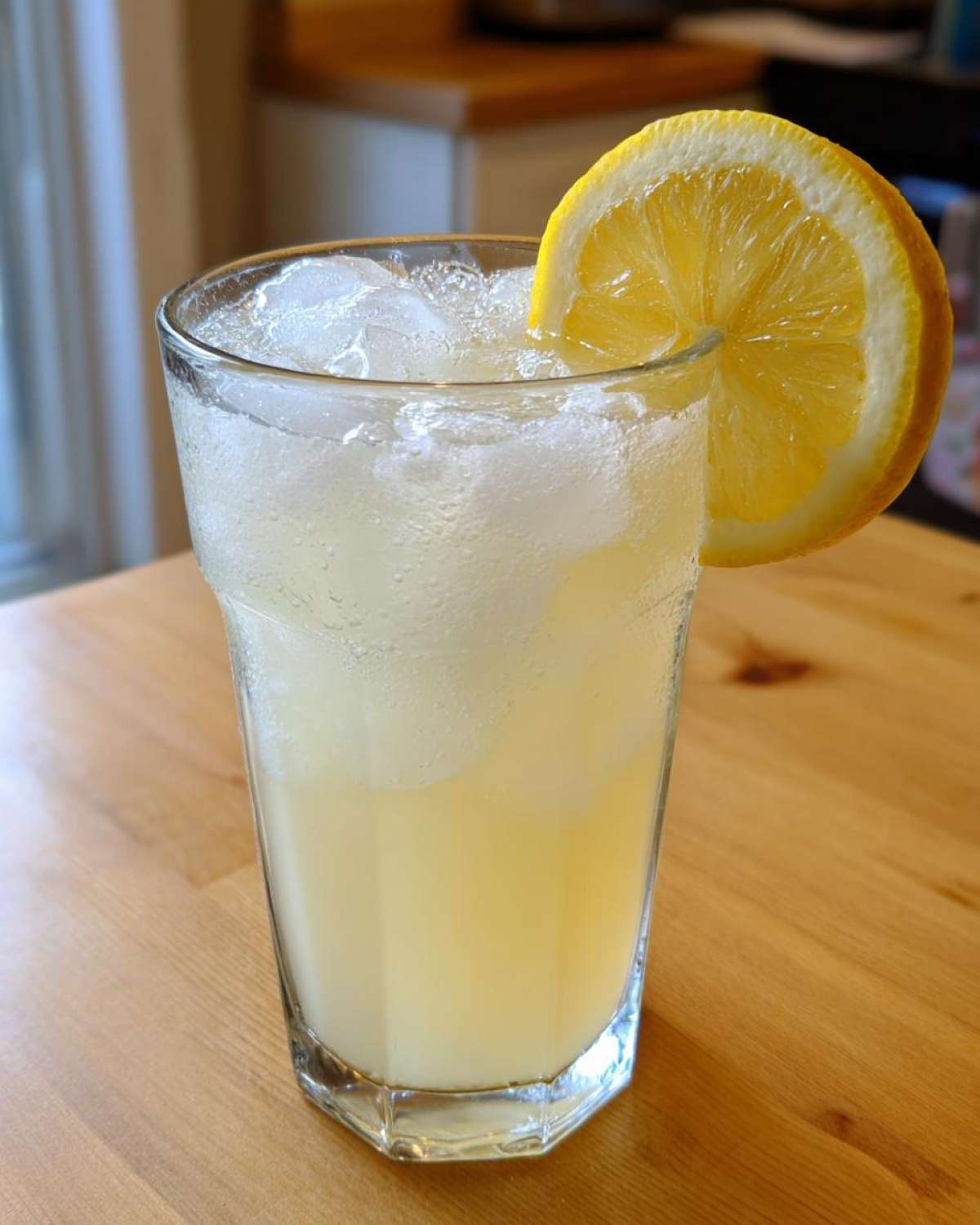A tall glass filled with ice and refreshing Old-Fashioned Homemade Lemonade, garnished with a fresh lemon slice.