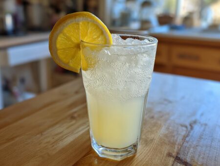 A tall glass filled with ice and sparkling Old-Fashioned Homemade Lemonade Recipe, garnished with a fresh lemon slice.