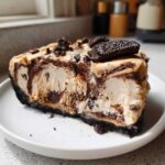 A thick slice of Peanut Butter Fudge Ice Cream Pie featuring a dark crust, creamy filling swirled with fudge, topped with crushed and whole Oreos.