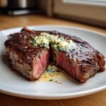 A perfectly grilled ribeye steak, sliced in half to show medium-rare interior, topped with melting garlic butter.