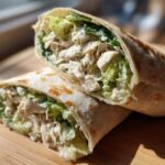 Two halves of a Quick Chicken Caesar Wrap filled with shredded chicken, romaine lettuce, and creamy Caesar dressing.