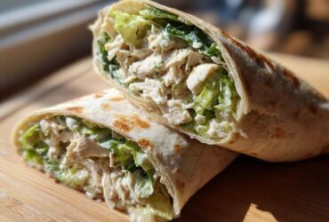Two halves of a Quick Chicken Caesar Wrap filled with shredded chicken, romaine lettuce, and creamy Caesar dressing.