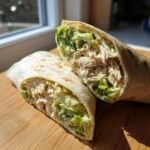 Two halves of a Quick Chicken Caesar Wraps for Lunch showing shredded chicken, romaine lettuce, and creamy dressing inside a tortilla.