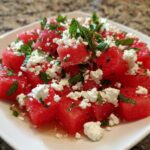 Close-up of a plate featuring Refreshing Watermelon Feta Salad with chunks of red watermelon, crumbled white feta cheese, and fresh mint leaves.