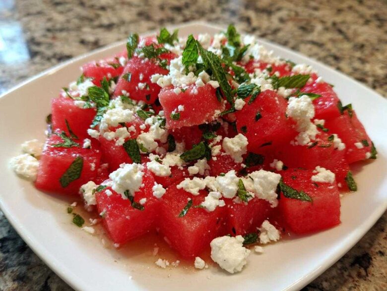 Close-up of a plate featuring Refreshing Watermelon Feta Salad with chunks of red watermelon, crumbled white feta cheese, and fresh mint leaves.