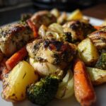 Close-up of golden-brown Sheet Pan Lemon Herb Roasted Chicken Pieces and Veggies, including potatoes, carrots, and broccoli.