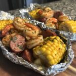 Close-up of cooked Shrimp Boil Foil Packets featuring seasoned shrimp, sliced sausage, and bright yellow corn on the cob.