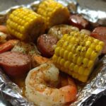 Close-up of cooked shrimp, sliced sausage, and corn on the cob seasoned in a foil packet for Shrimp Boil Foil Packets.