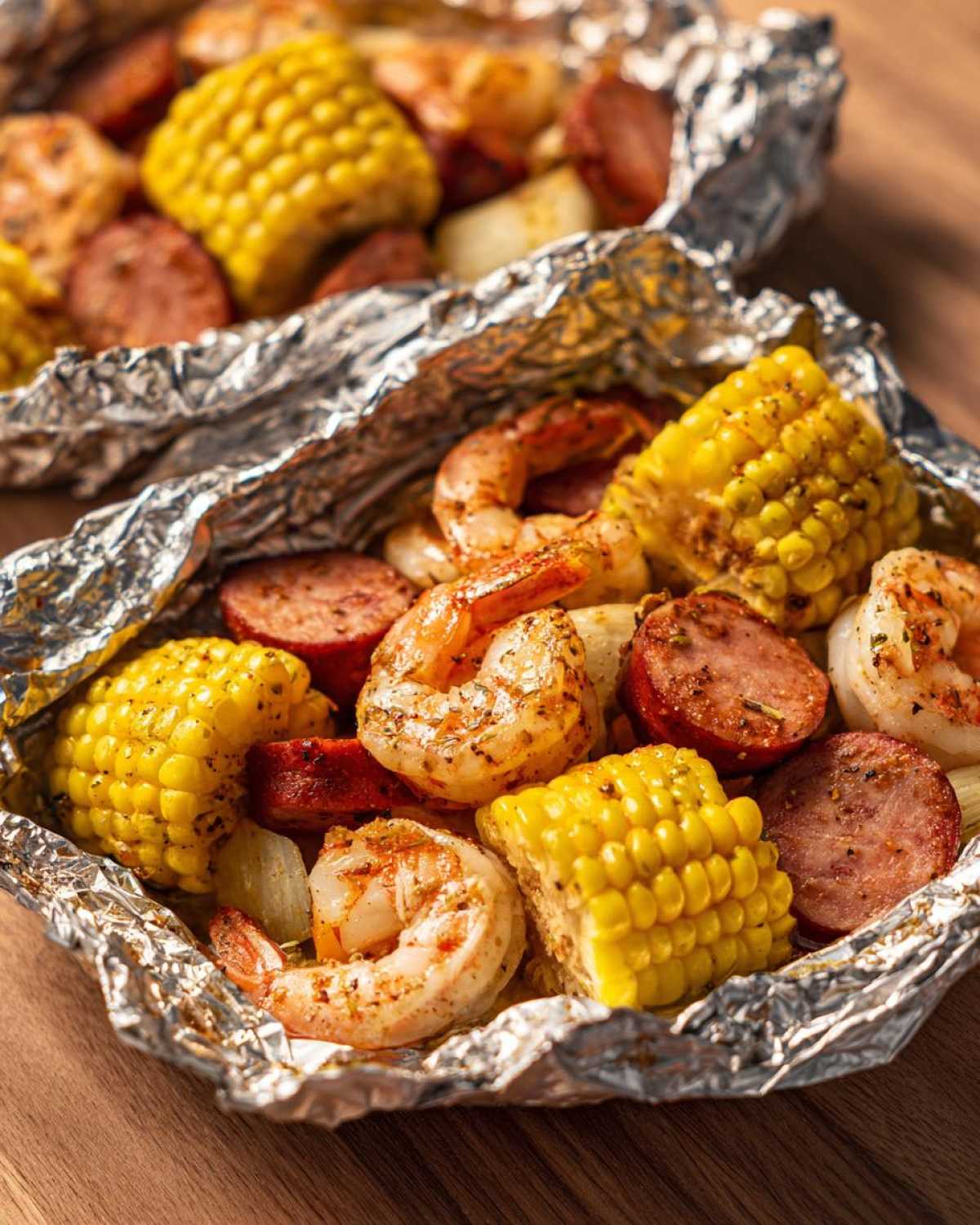 Close-up of cooked shrimp, sliced sausage, and corn on the cob served in opened Shrimp Boil Foil Packets.